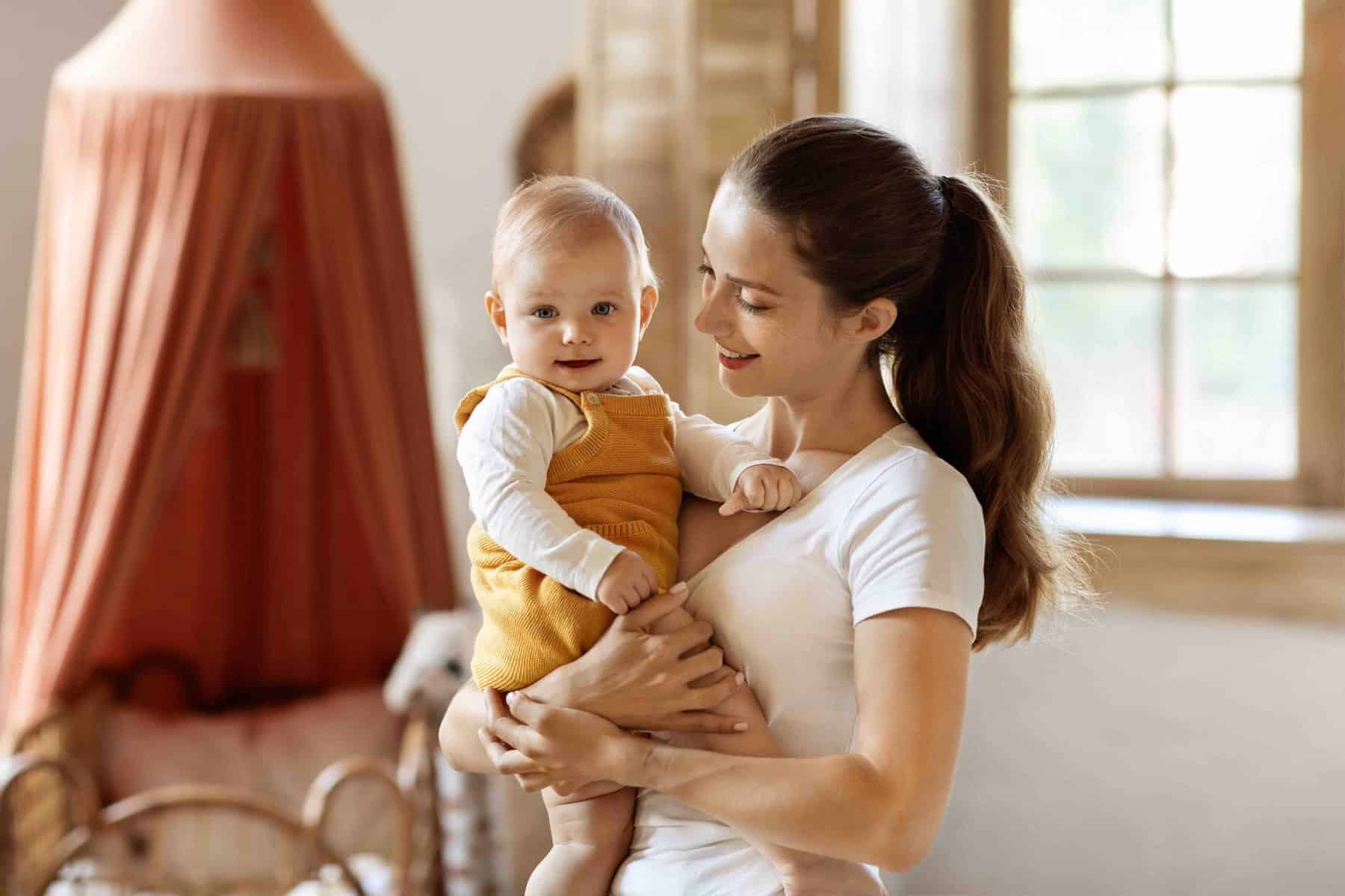Happy mother enjoying time with adorable toddler son at home Unconditional love. Happy young mother enjoying time with her adorable toddler son at home, mom holding child in her arms and smiling, playing with kid boy in lkids room, free space